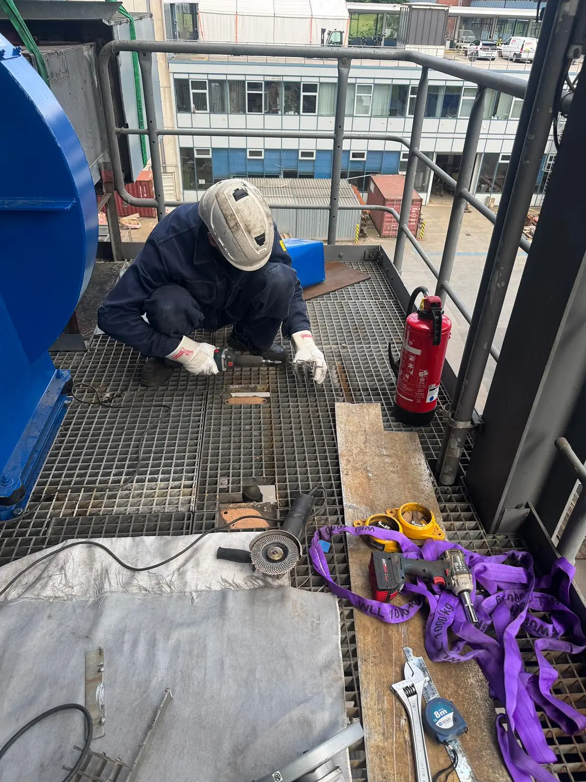 Operatore alla base del ventilatore appena calato sulla piattaforma a grigliato, con brache, attrezzi ed estintore disposti accanto a lui
