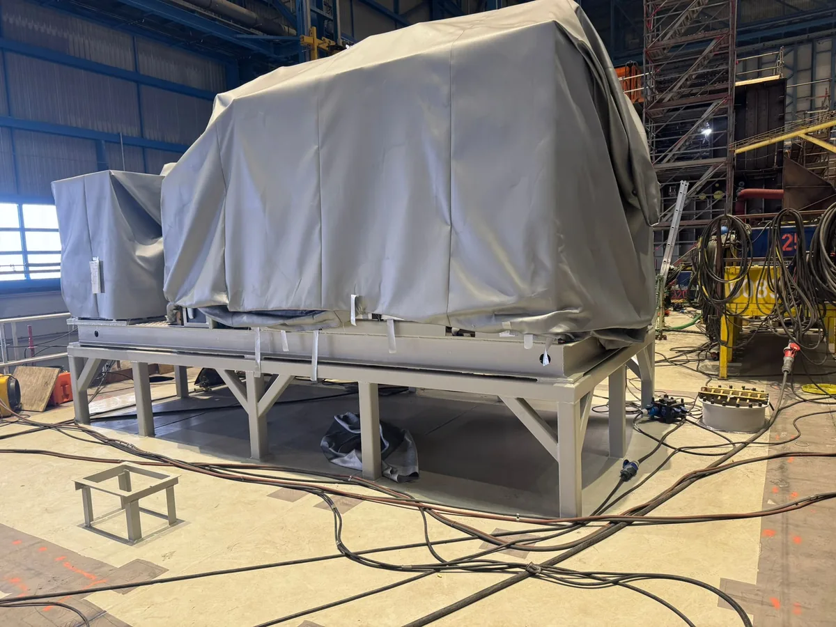 Gruppo macchina sotto teli di protezione su un telaio in acciaio costruito, in un capannone del cantiere navale