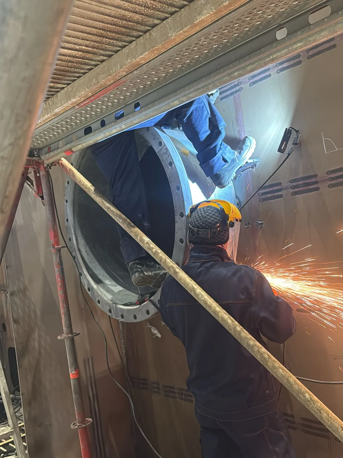 Due montatori a un attraversamento di paratia, uno verifica l’allineamento all’interno dell’apertura mentre l’altro rifinisce il lembo con la smerigliatrice