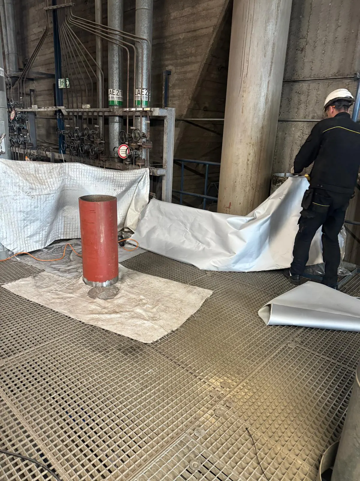 Schutzplanen und Schweißdecken über dem Gitterrost der Anlage, rund um einen zum Einbau bereitstehenden Rohrspool