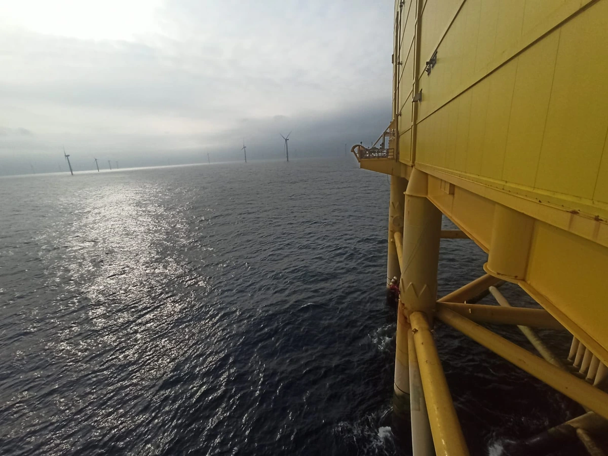 Flanc d’une plateforme offshore au-dessus de la mer, éoliennes dans les nuages bas à l’horizon